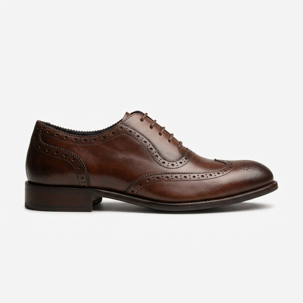 A single brown leather wingtip oxford shoe with brogue detailing, shown in a side profile on a light gray background.