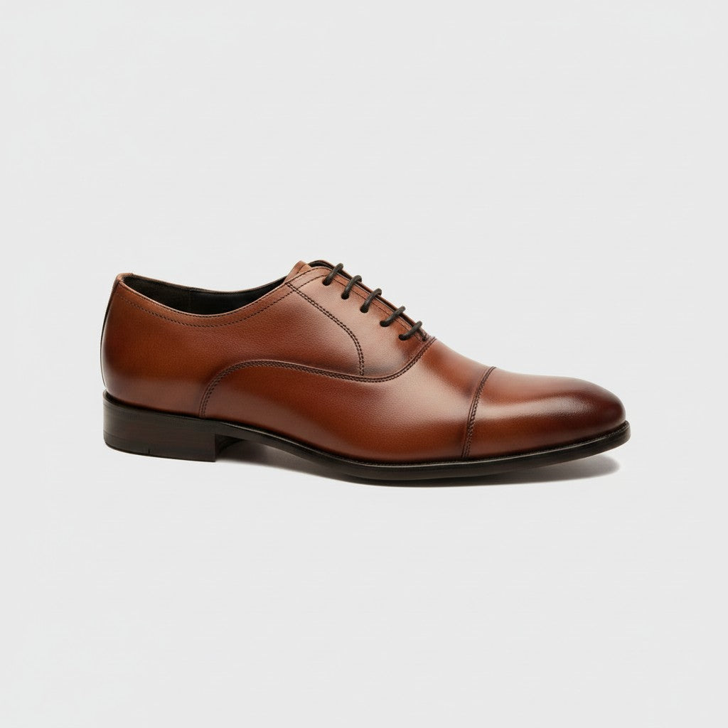 A classic brown leather cap-toe oxford shoe with black laces, shown in a side profile on a light gray background.