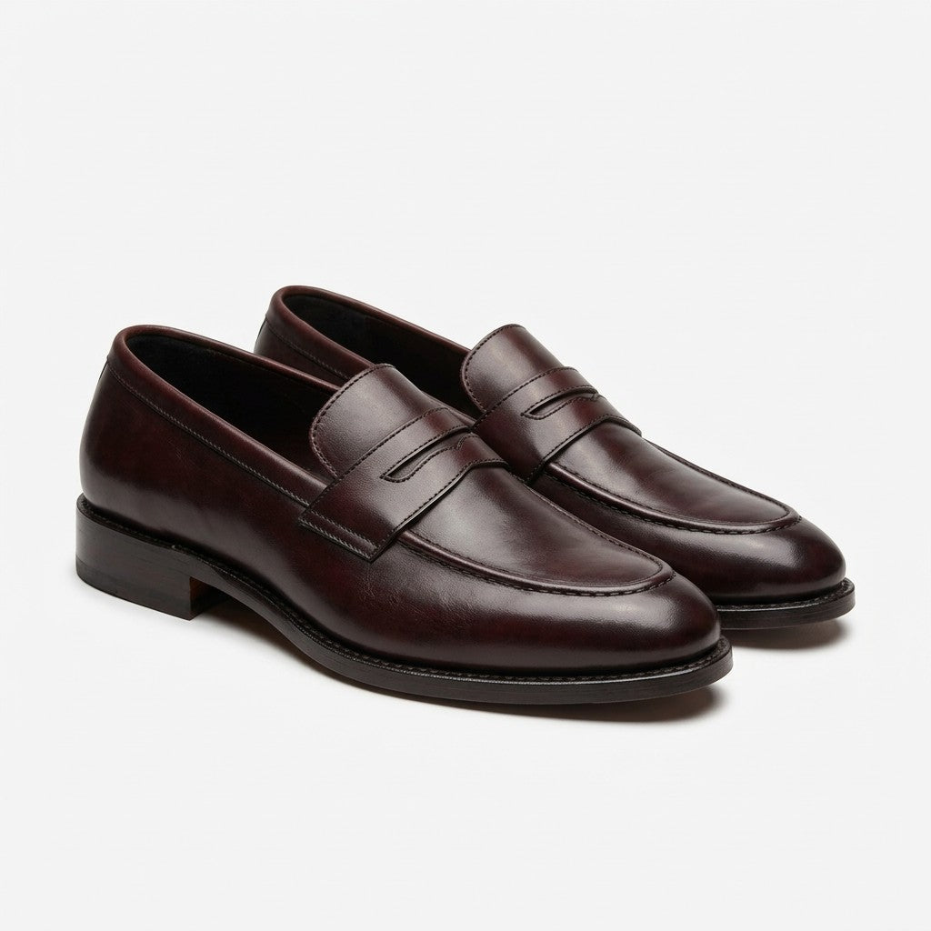 A pair of dark brown leather penny loafers with a smooth finish, displayed on a clean light gray background.