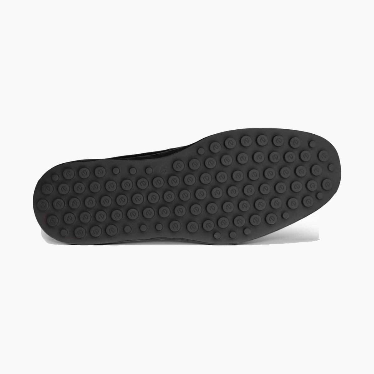 The black rubber outsole of a slip-on shoe, showing a pattern of circular tread knobs, photographed from a top-down view on a light gray background.